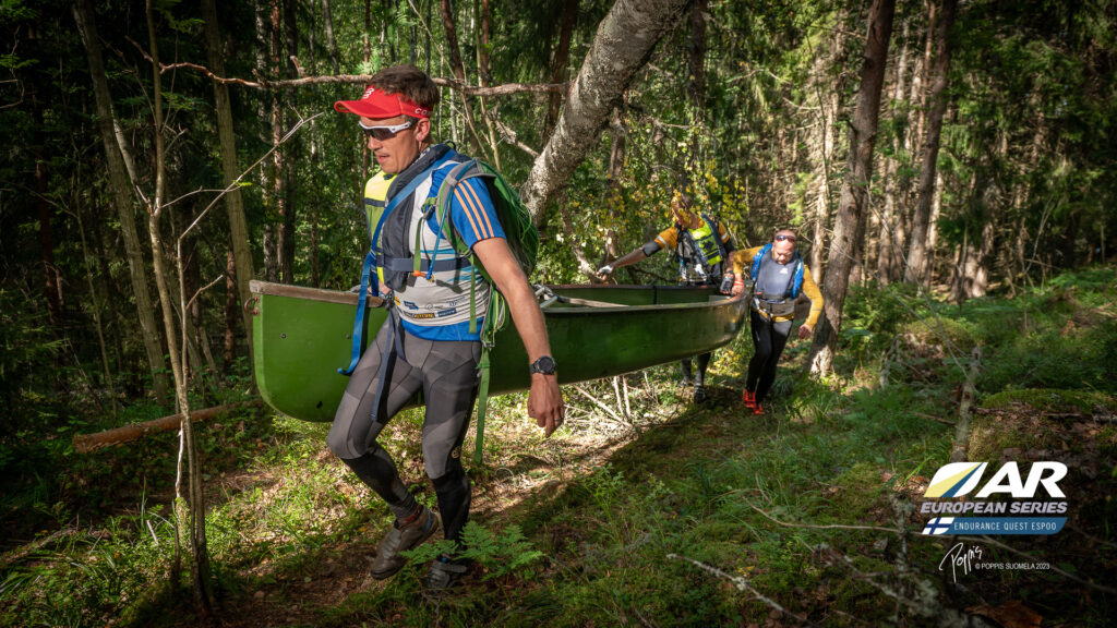 Kaksi melojaa kantaa kajakkia metsässä